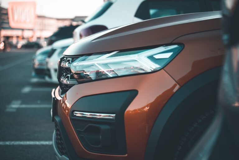 Close-up of a modern car's headlight in a parking lot at dusk, showcasing design and details.