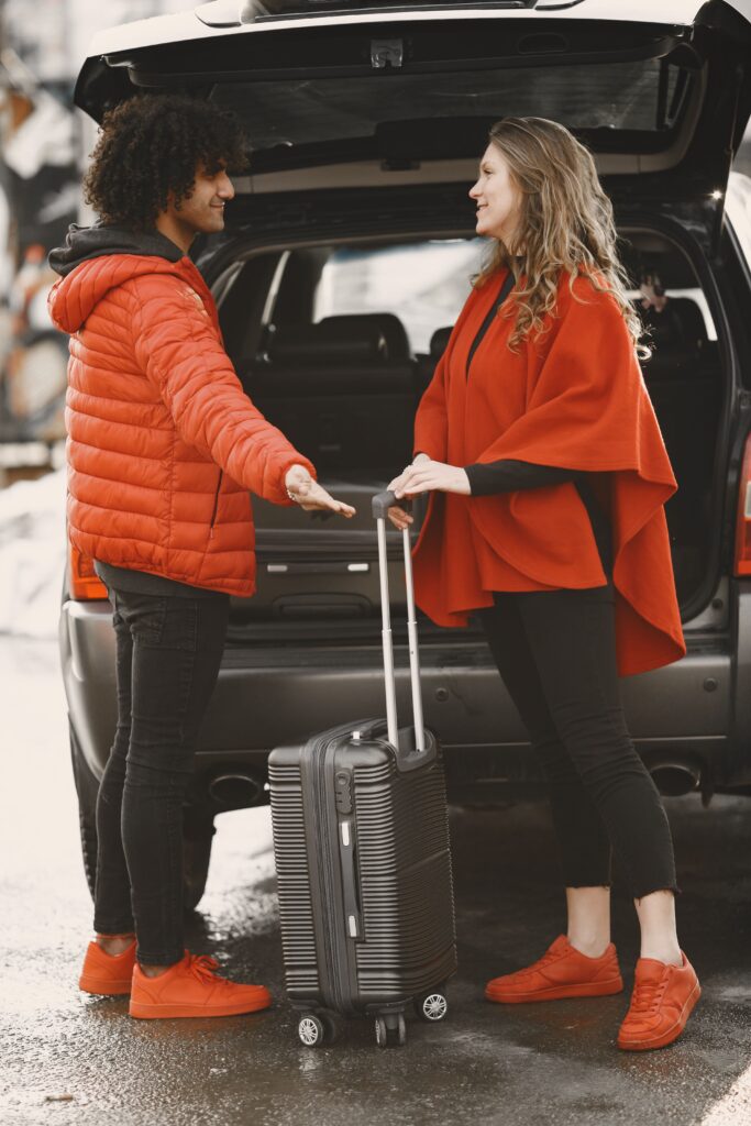 A couple stands by their car, packing luggage for a road trip.